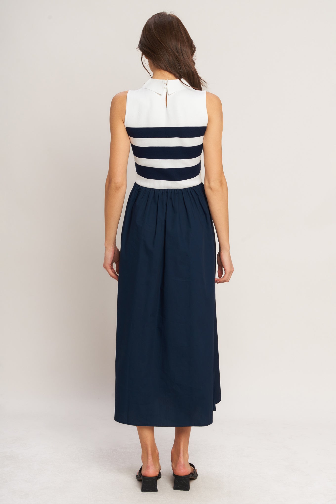 Woman wearing a sleeveless dress with white top and navy skirt on a plain background