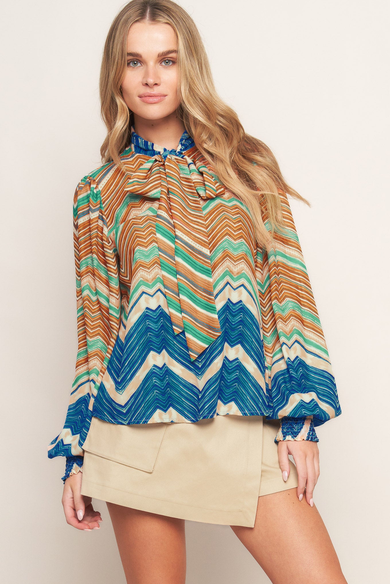 A printed woven top featuring high neckline with back neck tie and long sleeve with smocked cuff