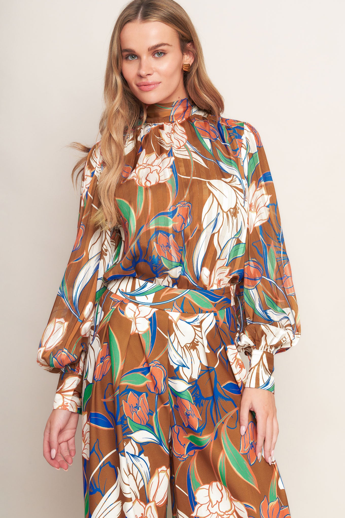 A printed woven top featuring a high neckline, blouson sleeve with cuff, and back neck tie closure.