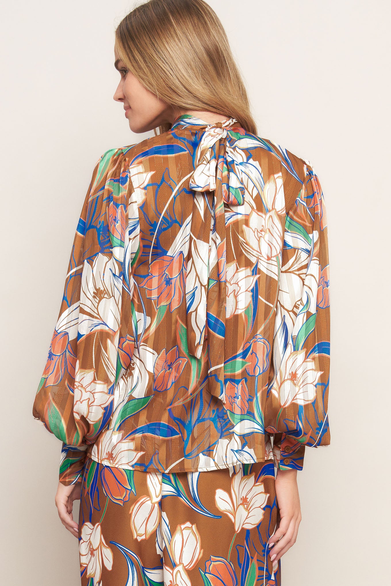 A printed woven top featuring a high neckline, blouson sleeve with cuff, and back neck tie closure.