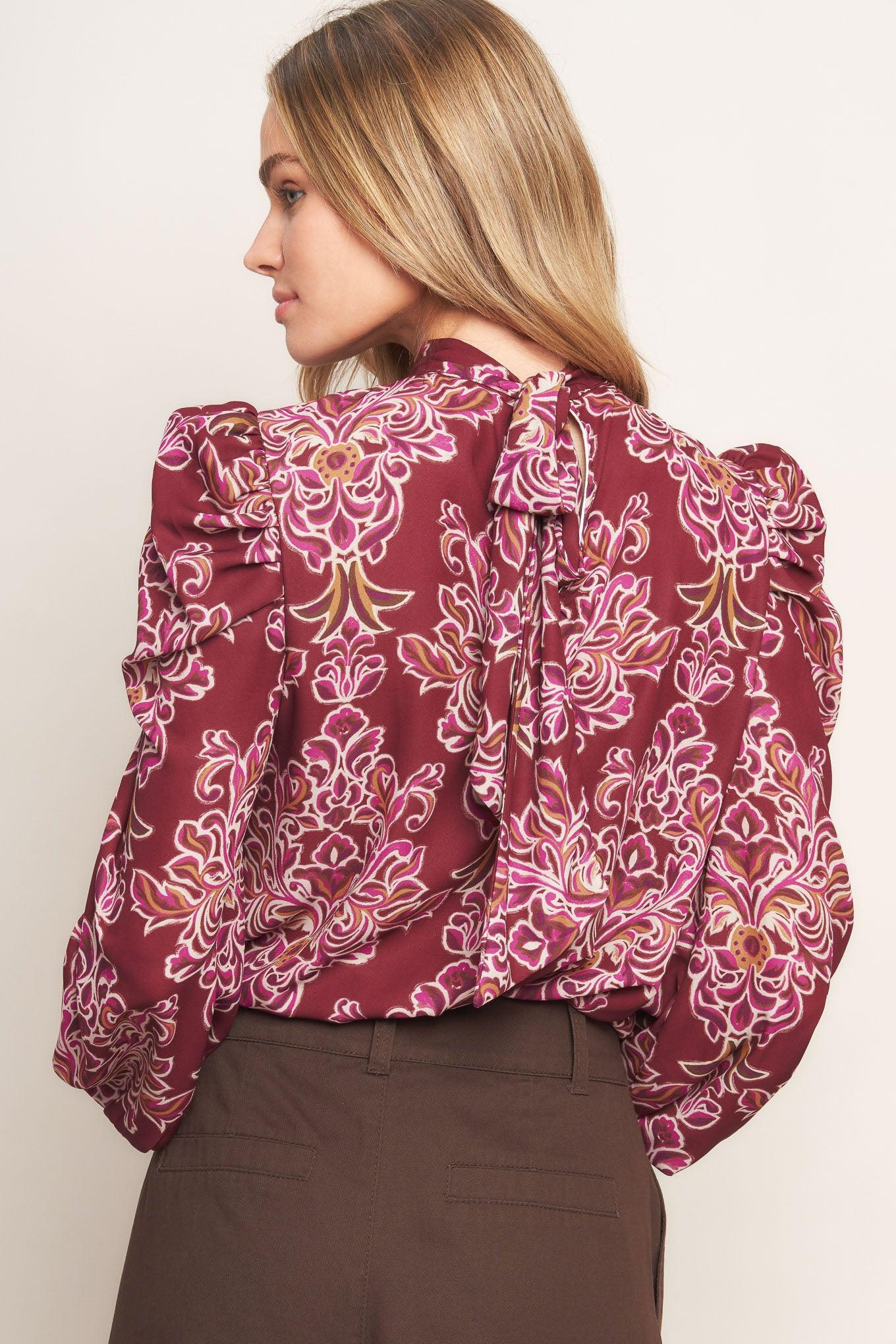 A printed woven top featuring high neckline, long puff sleeve and back neck tie closure
