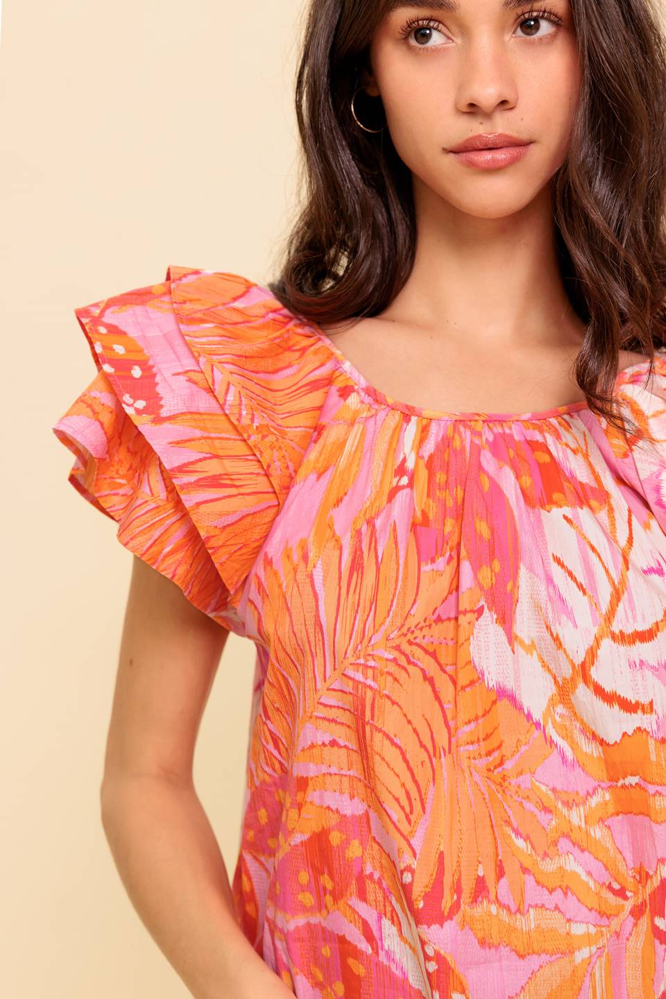 A printed woven top featuring round neckline, layered flutter sleeve and back neck button closure