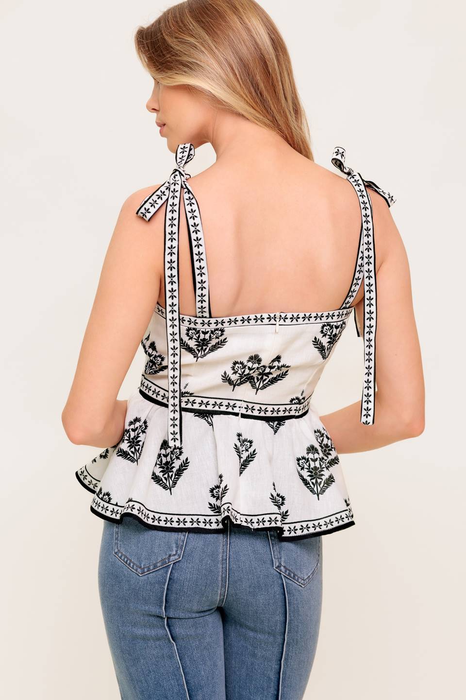 A printed woven top featuring straight neckline, shoulder tie, peplum and back zipper closure.