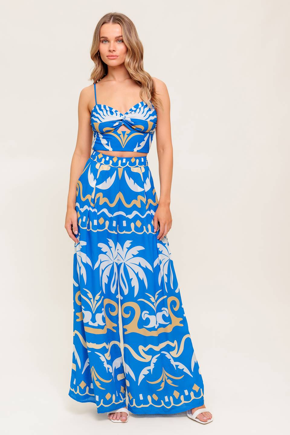 A printed woven crop top and pant set. Top featuring sweetheart neckline, straps, twisted front with cut out and smocked back bodice. Matching wide pant with side zipper closure.
