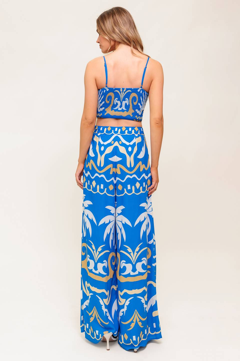 A printed woven crop top and pant set. Top featuring sweetheart neckline, straps, twisted front with cut out and smocked back bodice. Matching wide pant with side zipper closure.