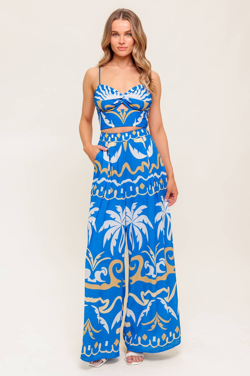 A printed woven crop top and pant set. Top featuring sweetheart neckline, straps, twisted front with cut out and smocked back bodice. Matching wide pant with side zipper closure.