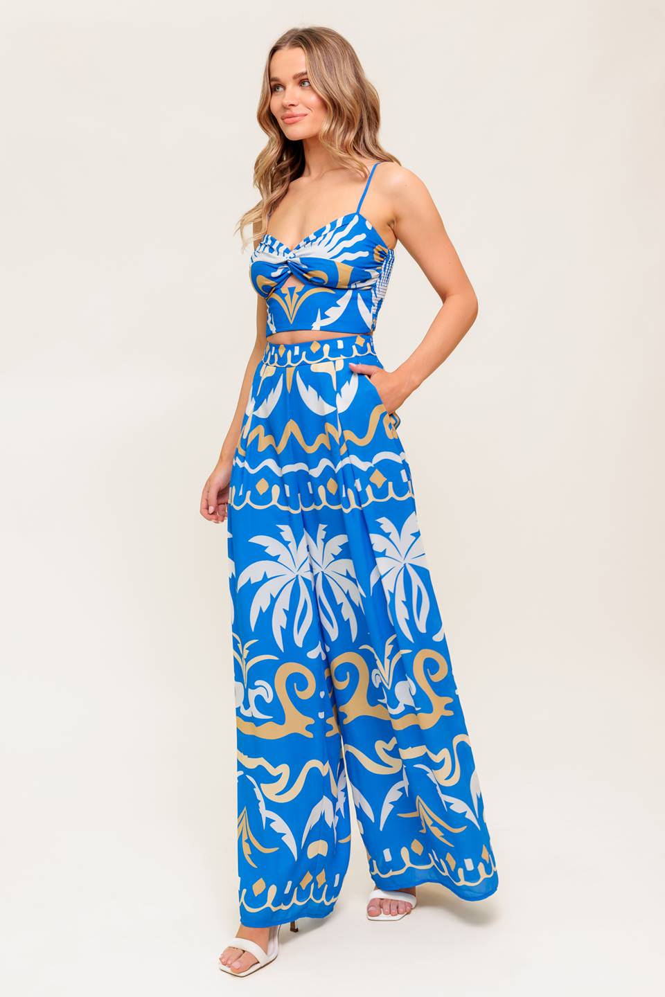 A printed woven crop top and pant set. Top featuring sweetheart neckline, straps, twisted front with cut out and smocked back bodice. Matching wide pant with side zipper closure.