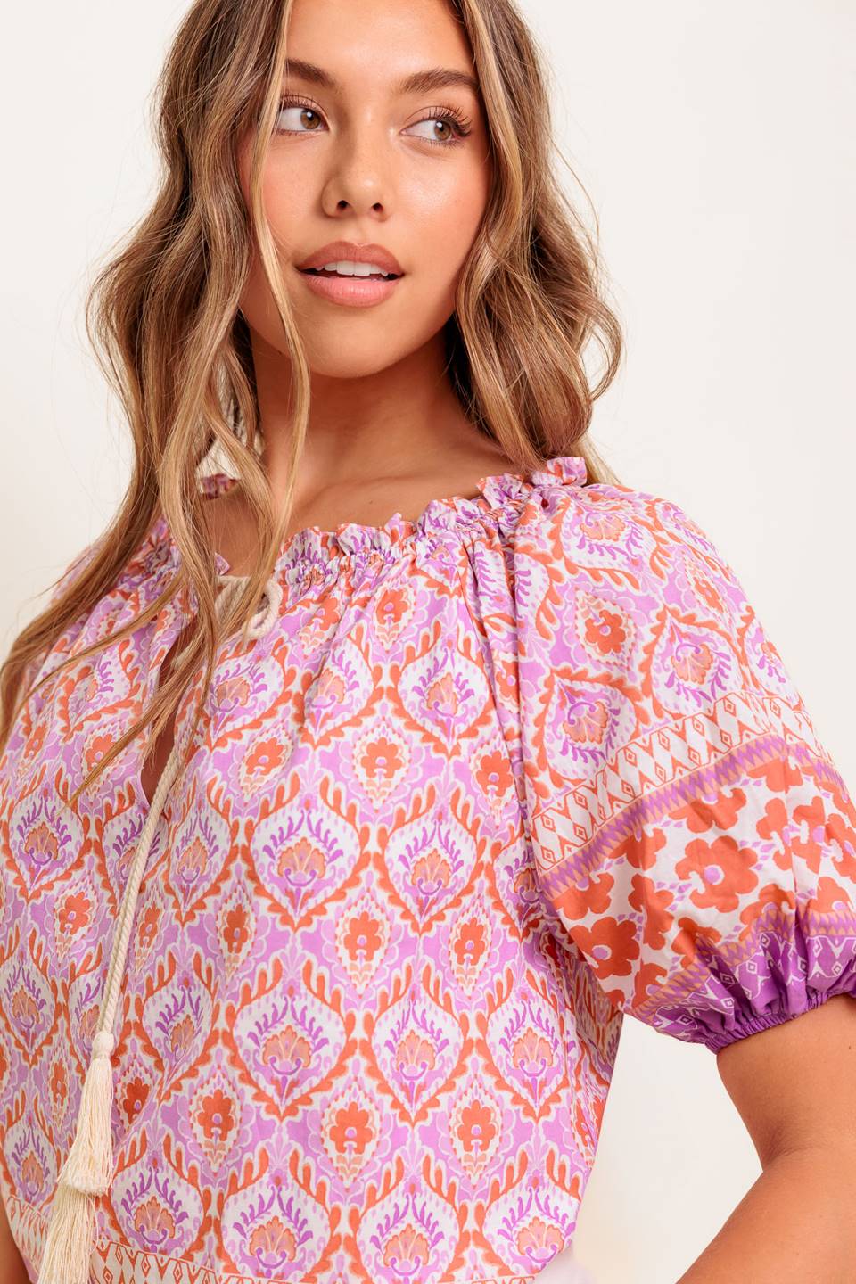 A printed woven top featuring wide neckline with ruffled edge, short sleeve and contrasting tie