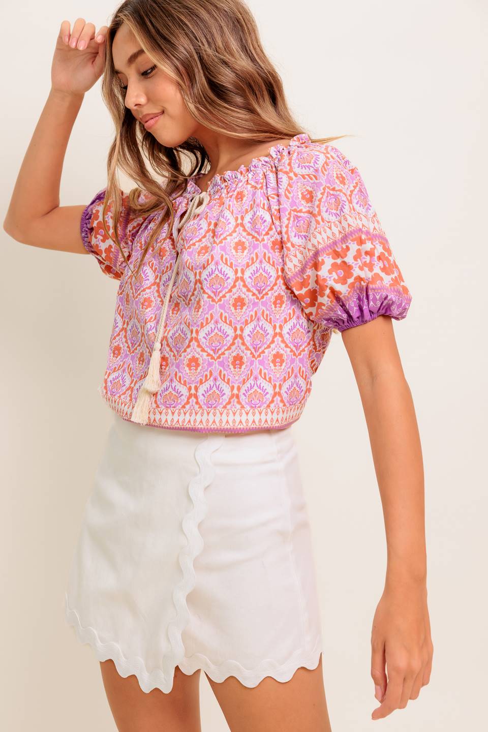 A printed woven top featuring wide neckline with ruffled edge, short sleeve and contrasting tie
