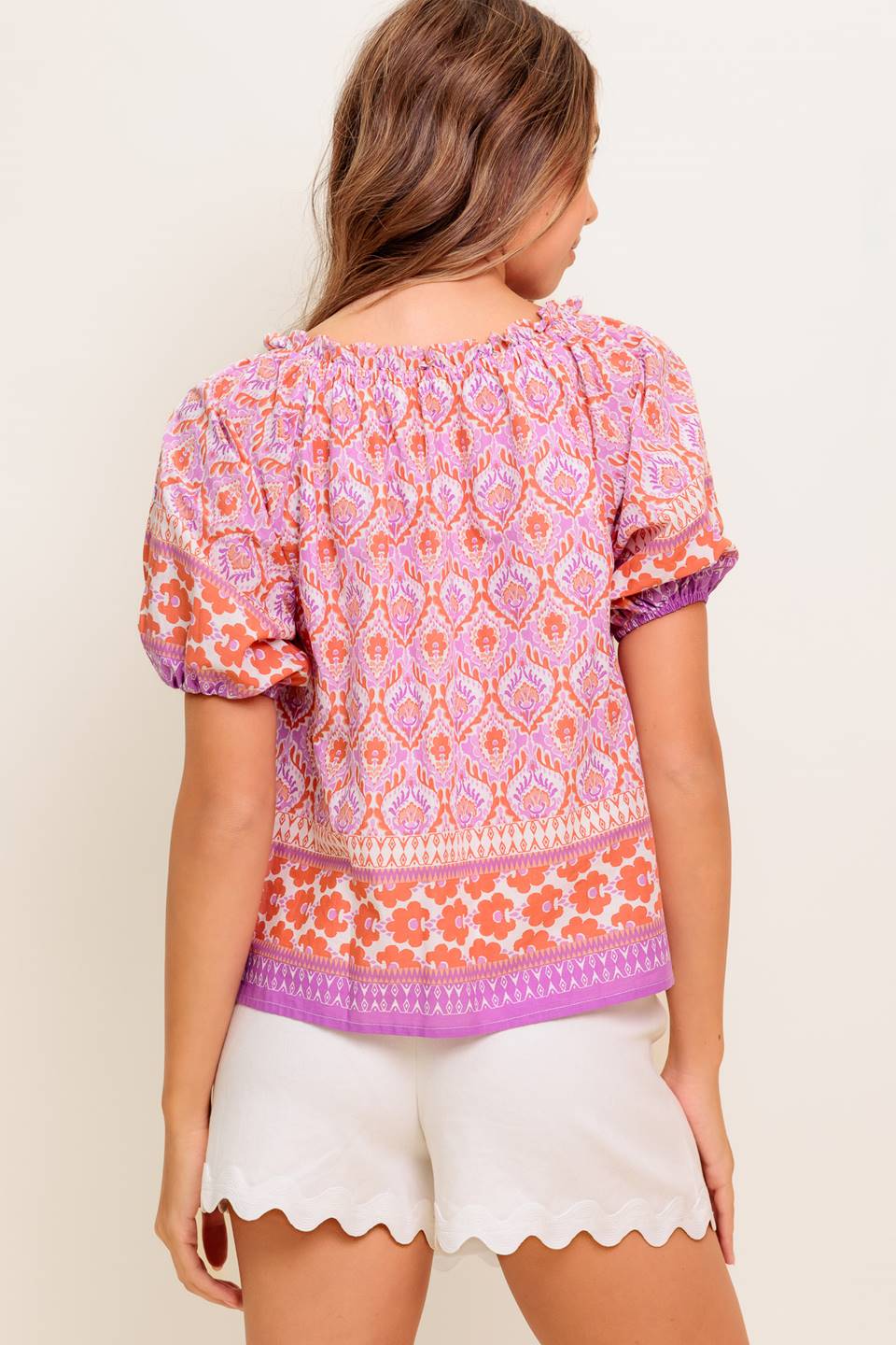 A printed woven top featuring wide neckline with ruffled edge, short sleeve and contrasting tie