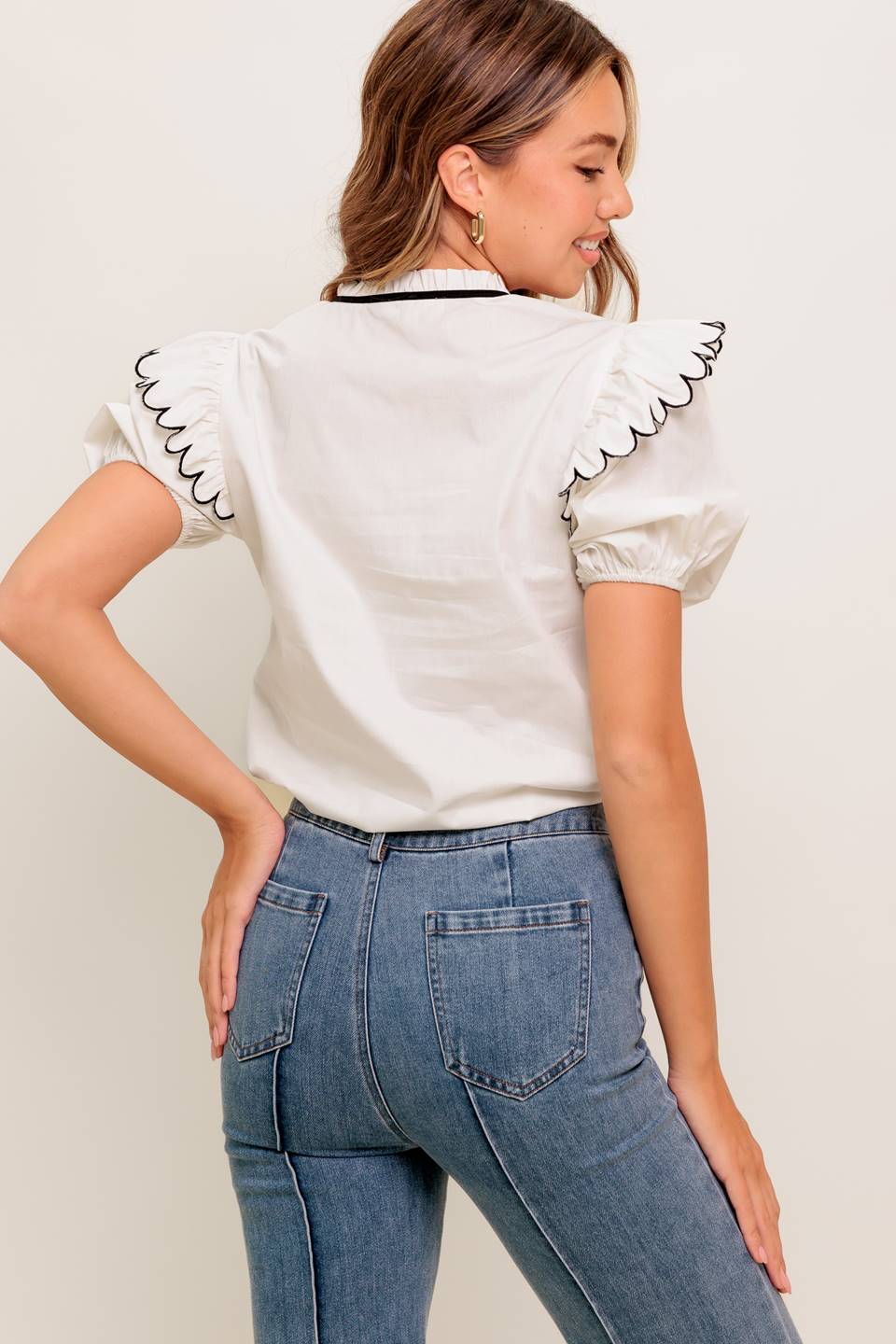 A solid woven top featuring ruffed neckline with tie, scallop edge shoulder and short sleeve