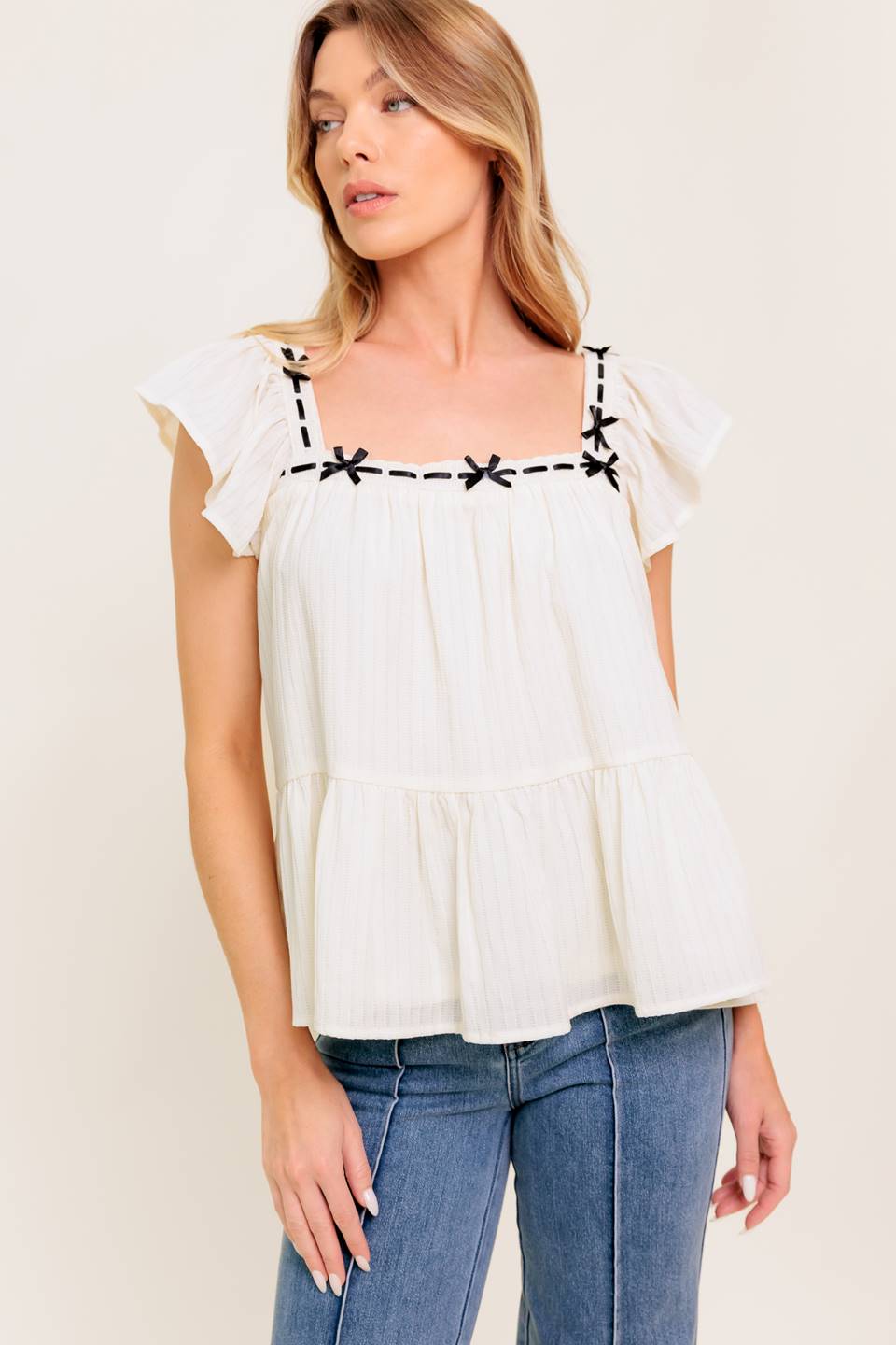 A solid woven top featuring square neckline, short flutter sleeve, ribbon trim and ruffled hemline.