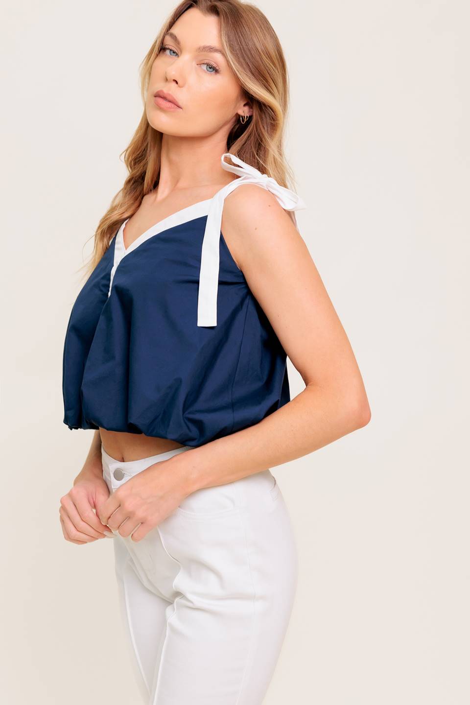 A solid woven top featuring shoulder tie, button detail and bubble hemline.
