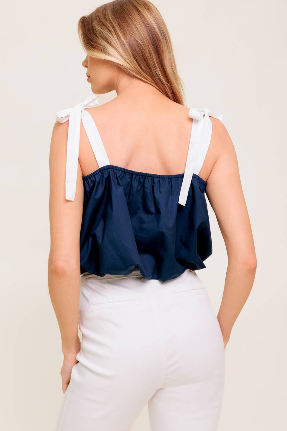 A solid woven top featuring shoulder tie, button detail and bubble hemline.