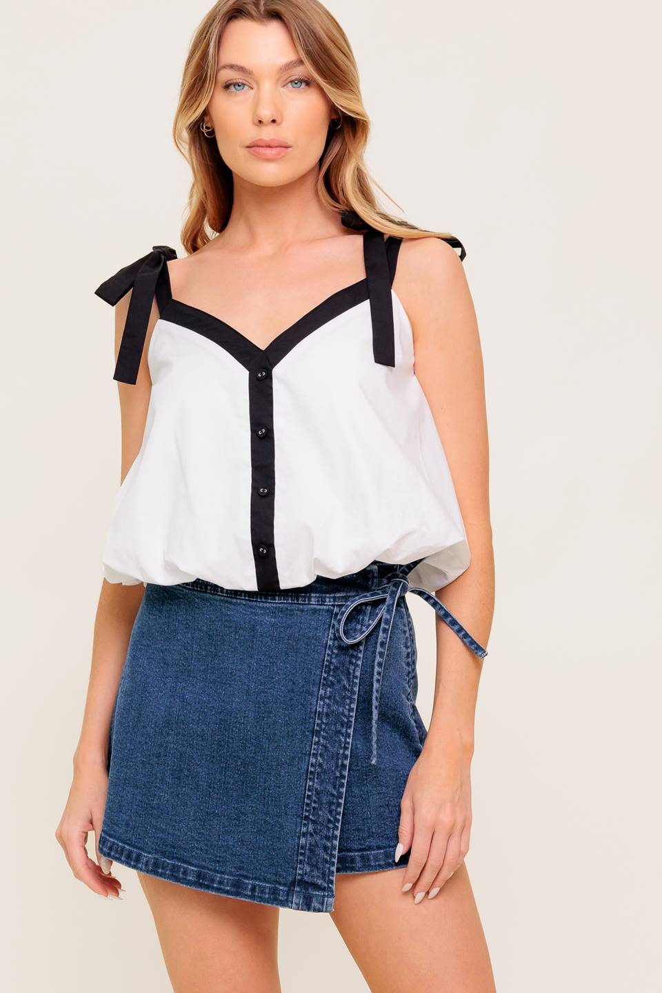A solid woven top featuring shoulder tie, button detail and bubble hemline.