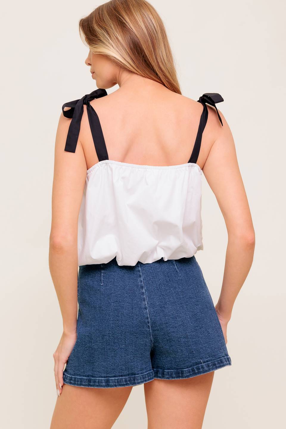 A solid woven top featuring shoulder tie, button detail and bubble hemline.