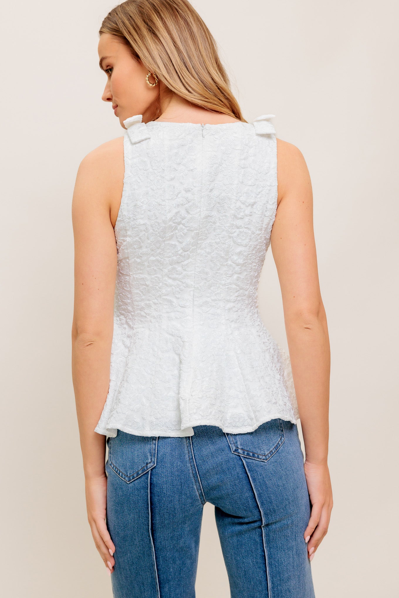 A texture woven top featuring round neckline, bow detail at shoulder, peplum and back zipper closure