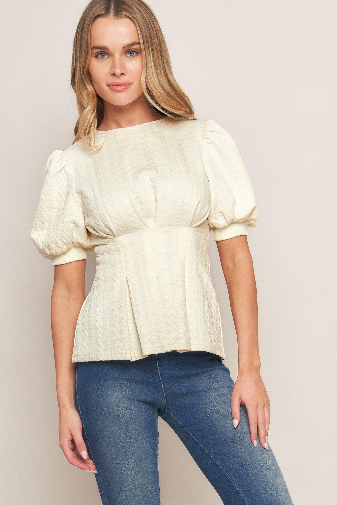 A textured woven top featuring round neckline, short puff sleeve, tapered waist and peplum