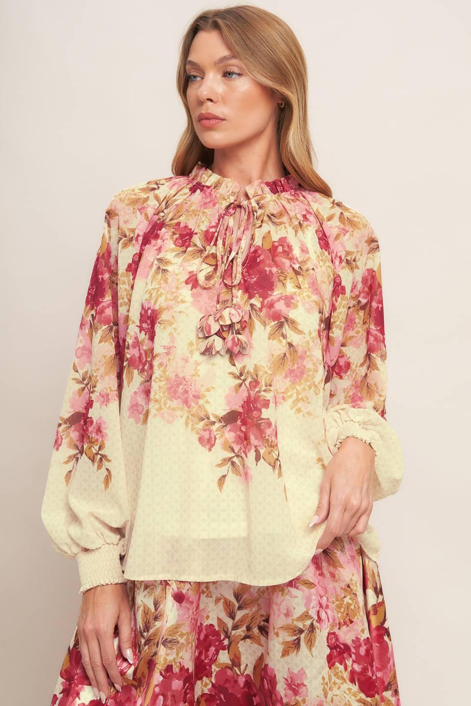 A printed woven top featuring ruffled neckline with front tie and long sleeve with smocked cuff