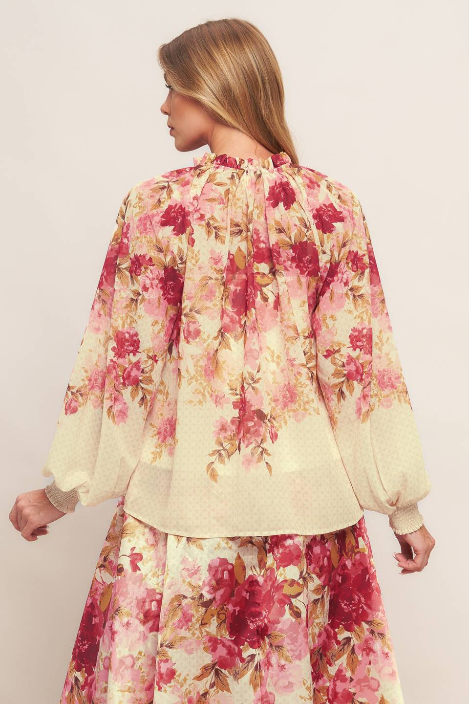 A printed woven top featuring ruffled neckline with front tie and long sleeve with smocked cuff
