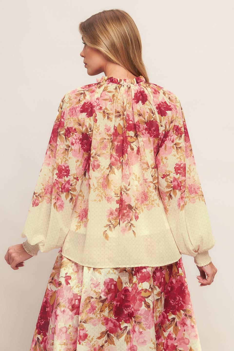 A printed woven top featuring ruffled neckline with front tie and long sleeve with smocked cuff