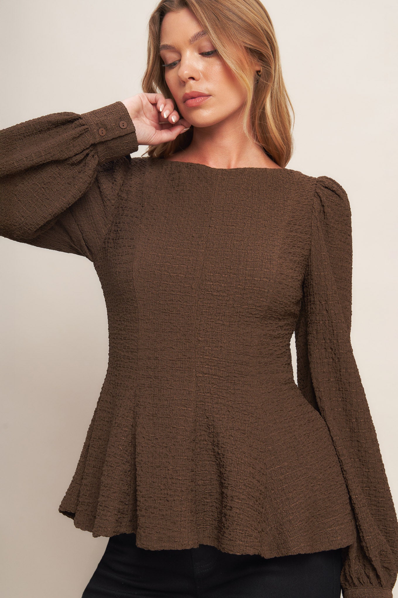 A textured woven top featuring round neckline, long sleeve, peplum and back zipper closure