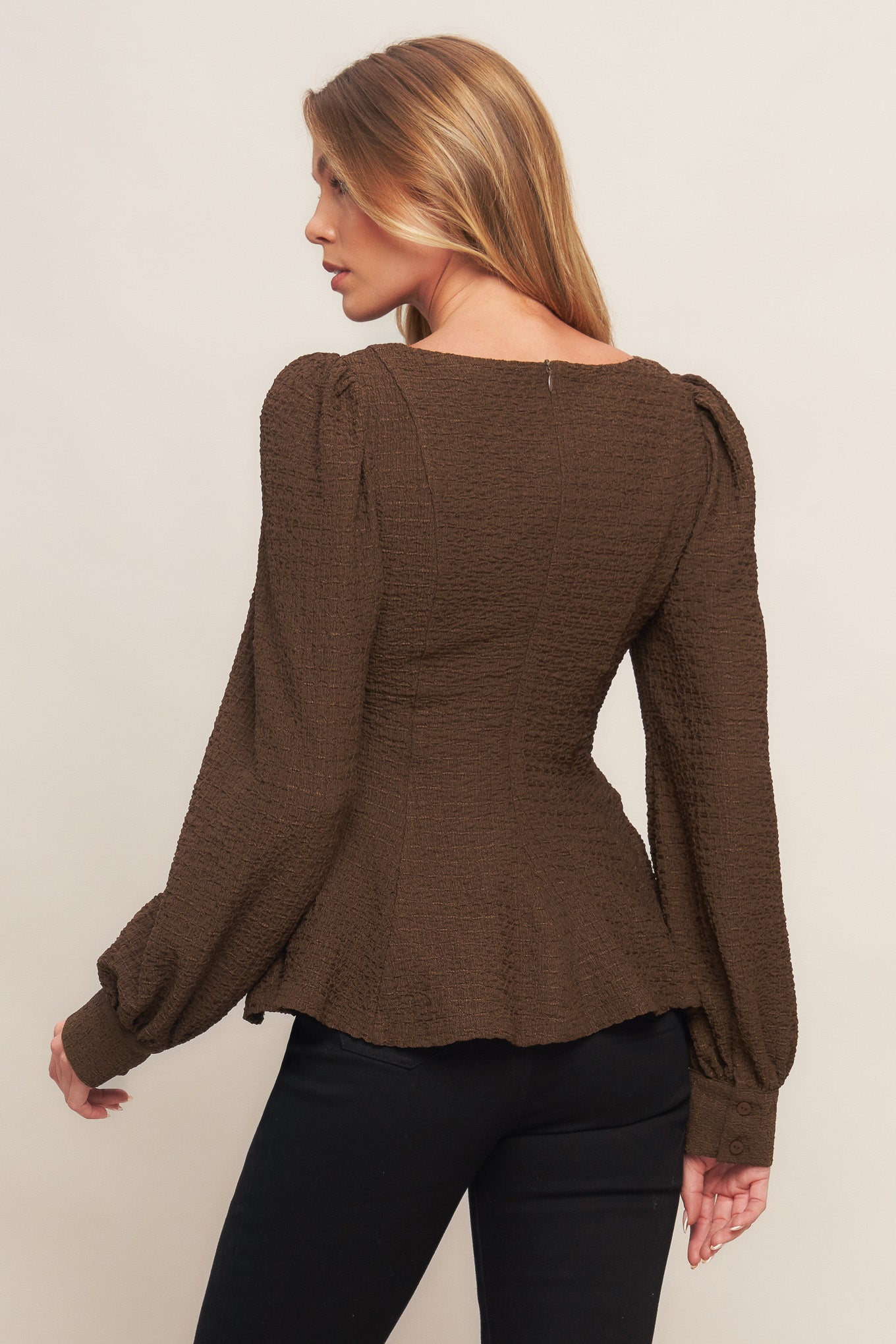 A textured woven top featuring round neckline, long sleeve, peplum and back zipper closure
