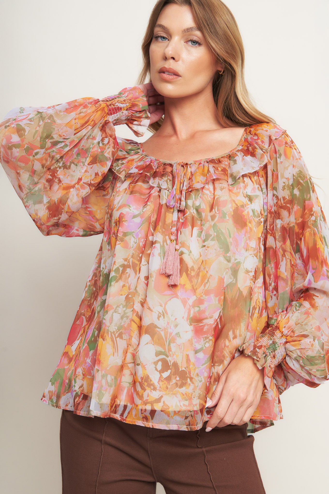 A printed woven top featuring wide round neckline with ruffles, front tie and tassel, long blouson sleeve with ruffled cuff and lining