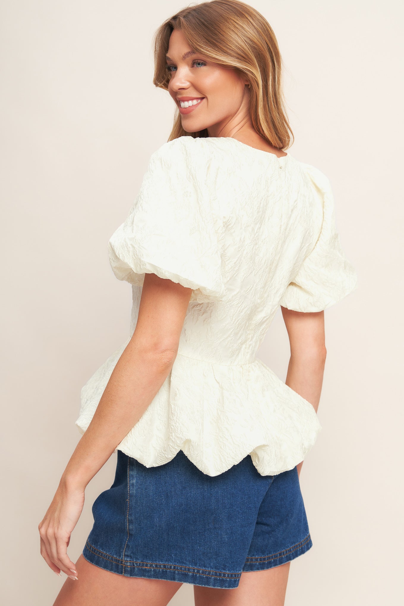 A textured woven top featuring round neckline, short puff sleeve, bubble peplum and back zipper closure