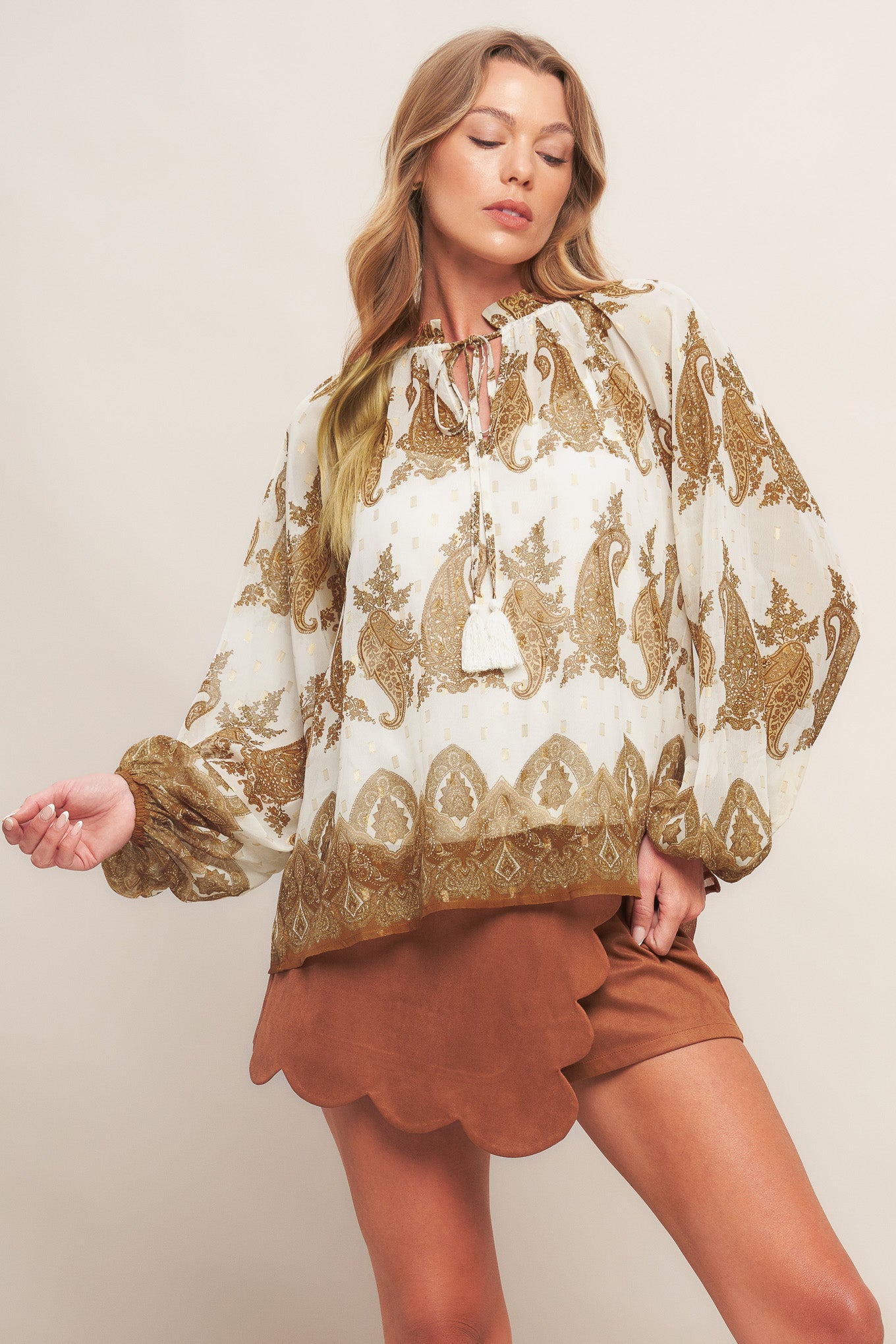A printed woven top featuring ruffled round neckline with front tie tassel and long sleeve