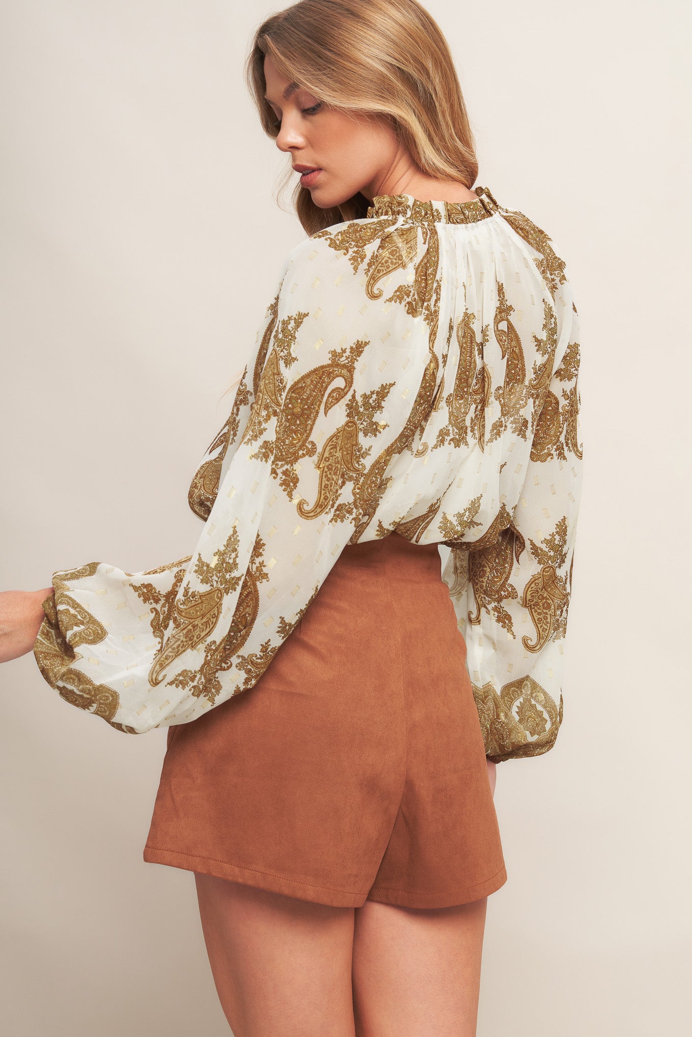 A printed woven top featuring ruffled round neckline with front tie tassel and long sleeve