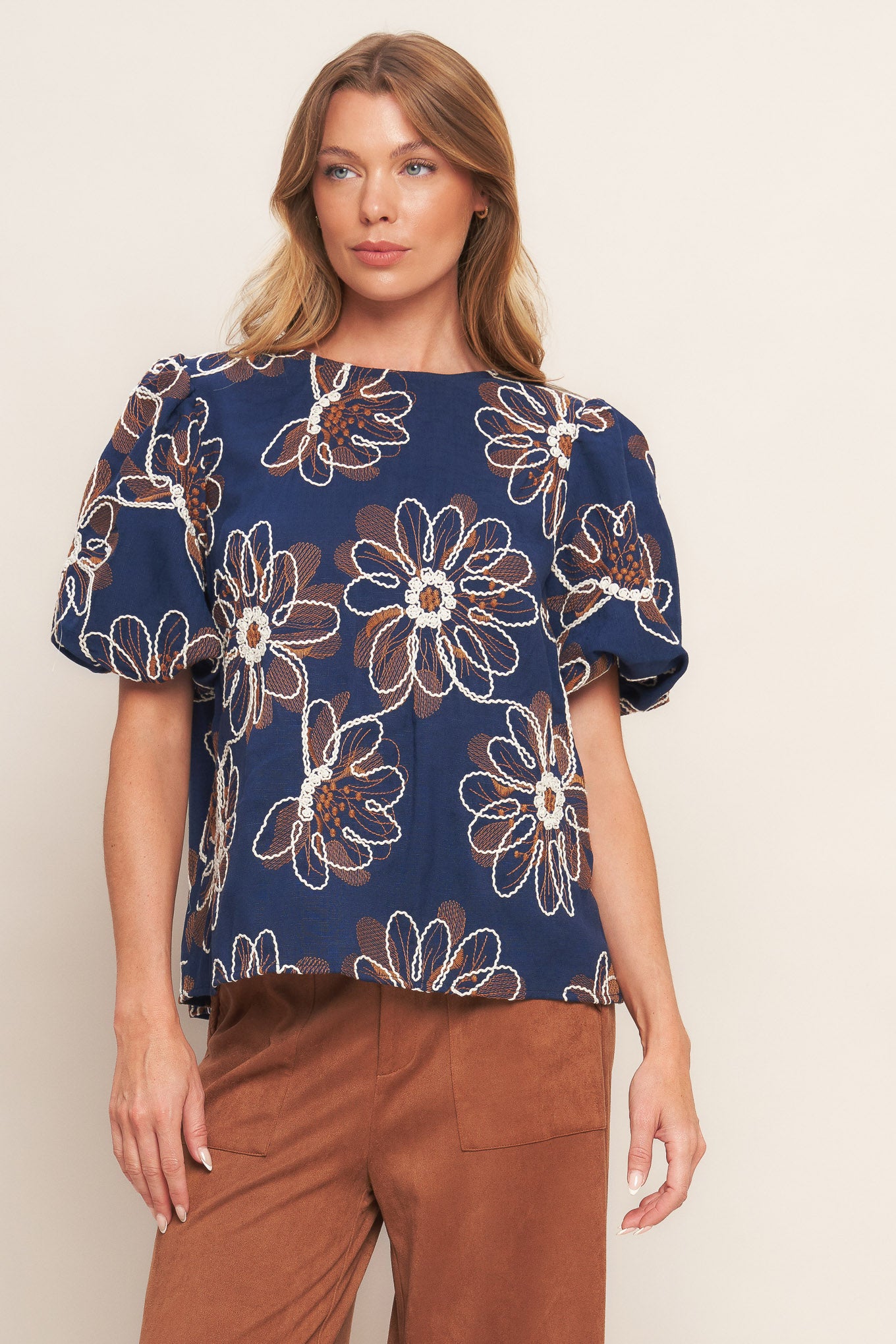 An embroidered woven top featuring round neckline, short puff sleeve and back neck button closure