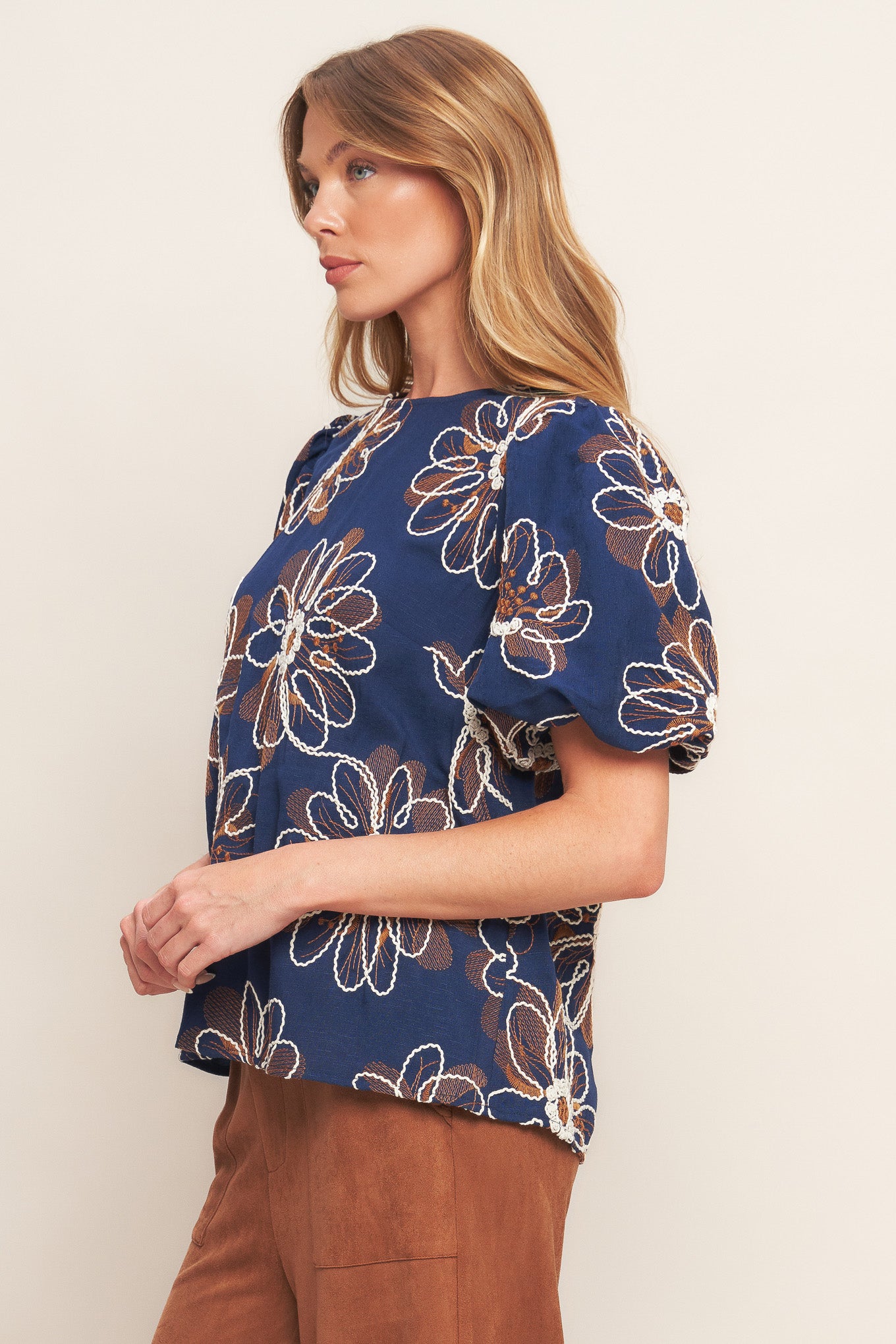 An embroidered woven top featuring round neckline, short puff sleeve and back neck button closure