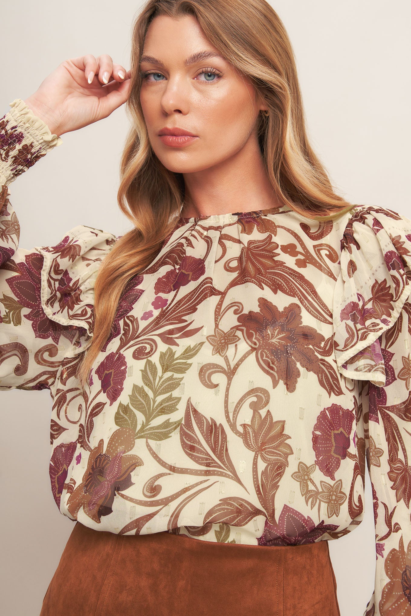A printed woven top featuring round neckline, long sleeve with cuff and ruffled shoulder and back neck button closure