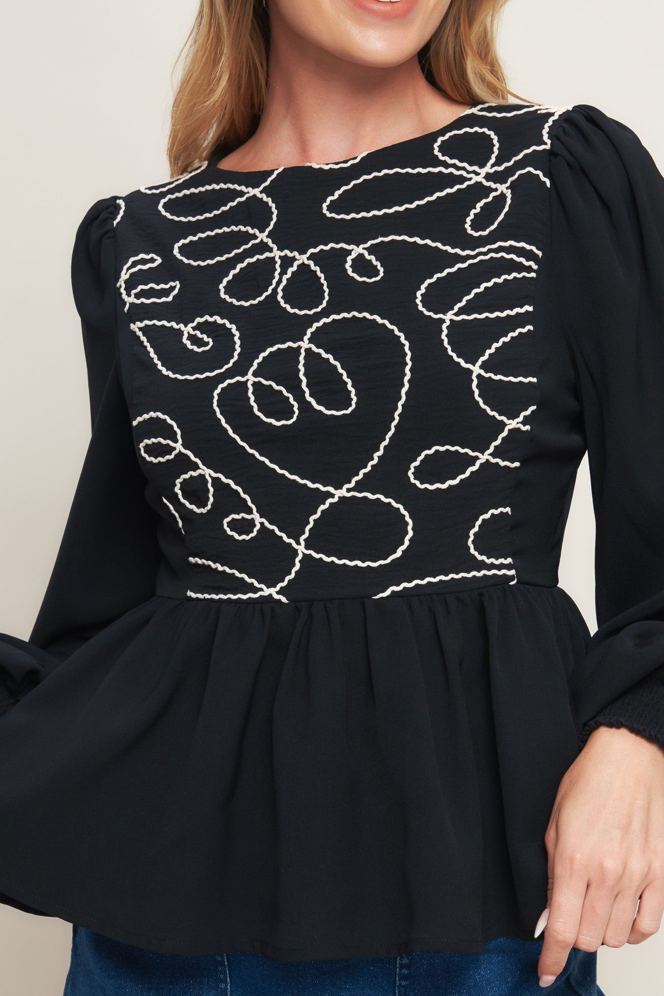 A solid woven top featuring round neckline, long sleeve, embellished bodice, peplum and back zipper closure