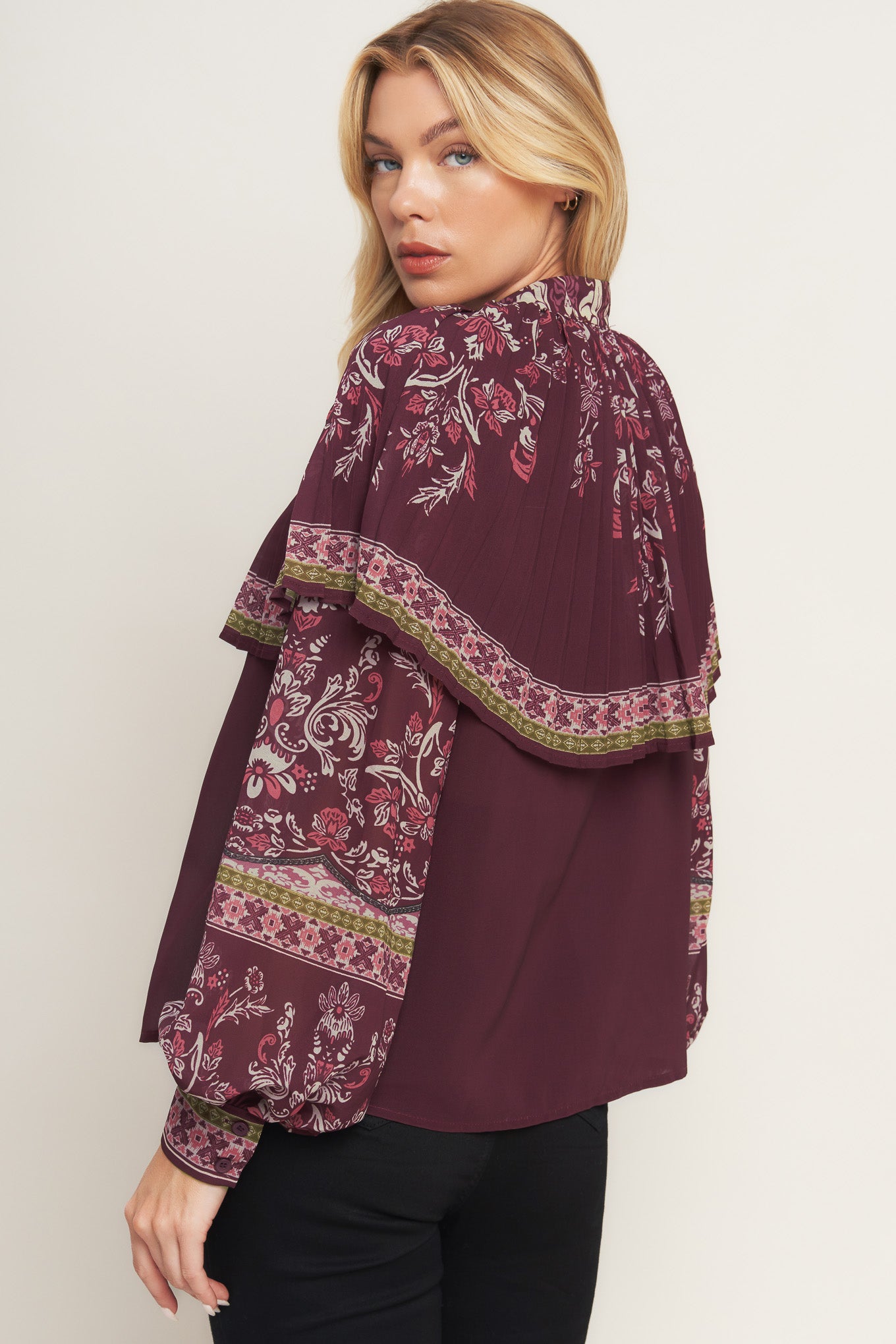 A printed woven top featuring pleated capelet, front bow tie, button down and long sleeve with cuff.