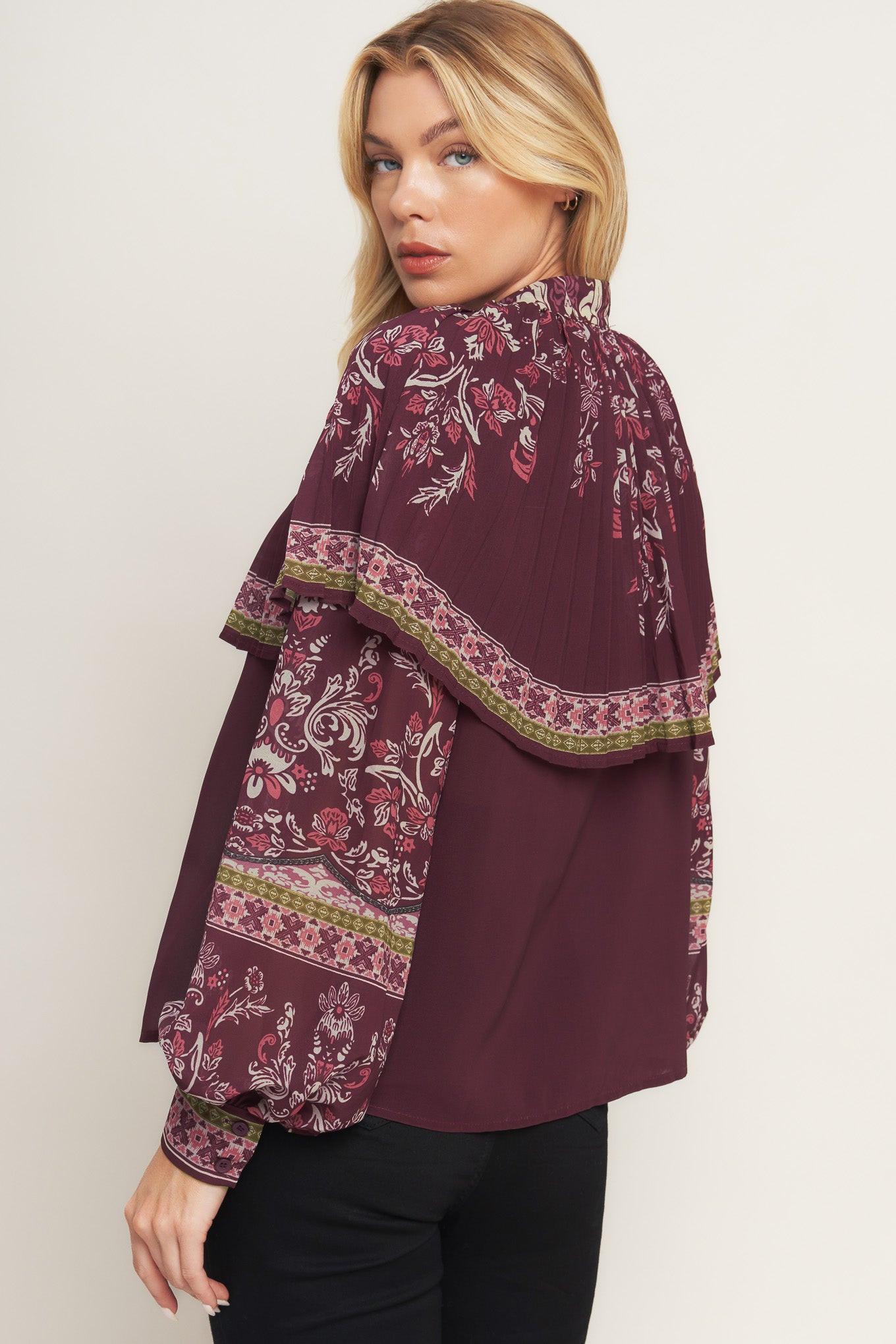A printed woven top featuring pleated capelet, front bow tie, button down and long sleeve with cuff.