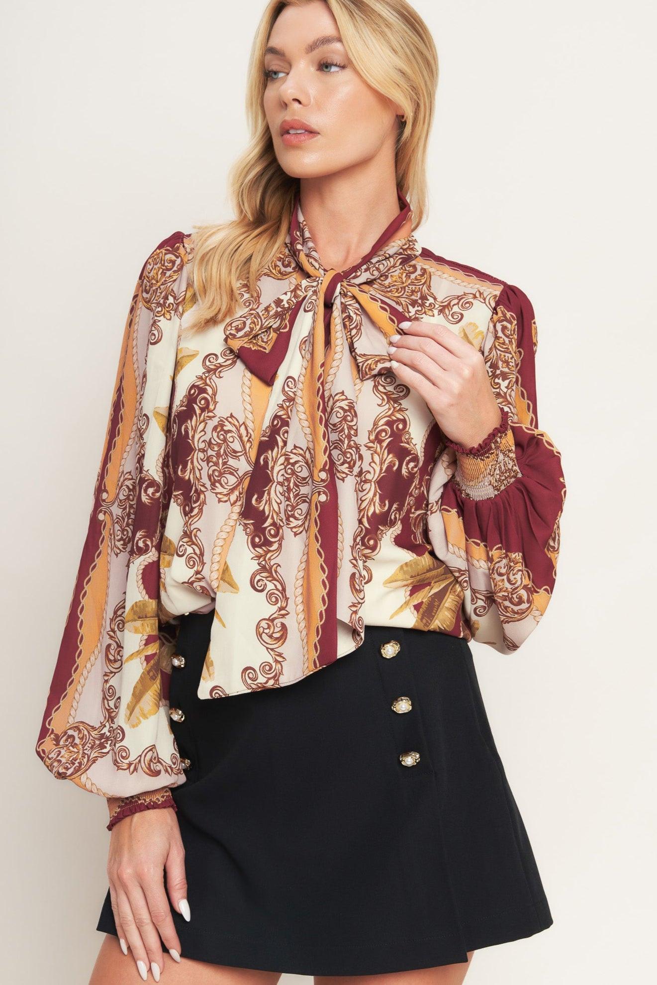 A printed woven top featuring front bow tie, long sleeve with smocked cuff and front button down closure