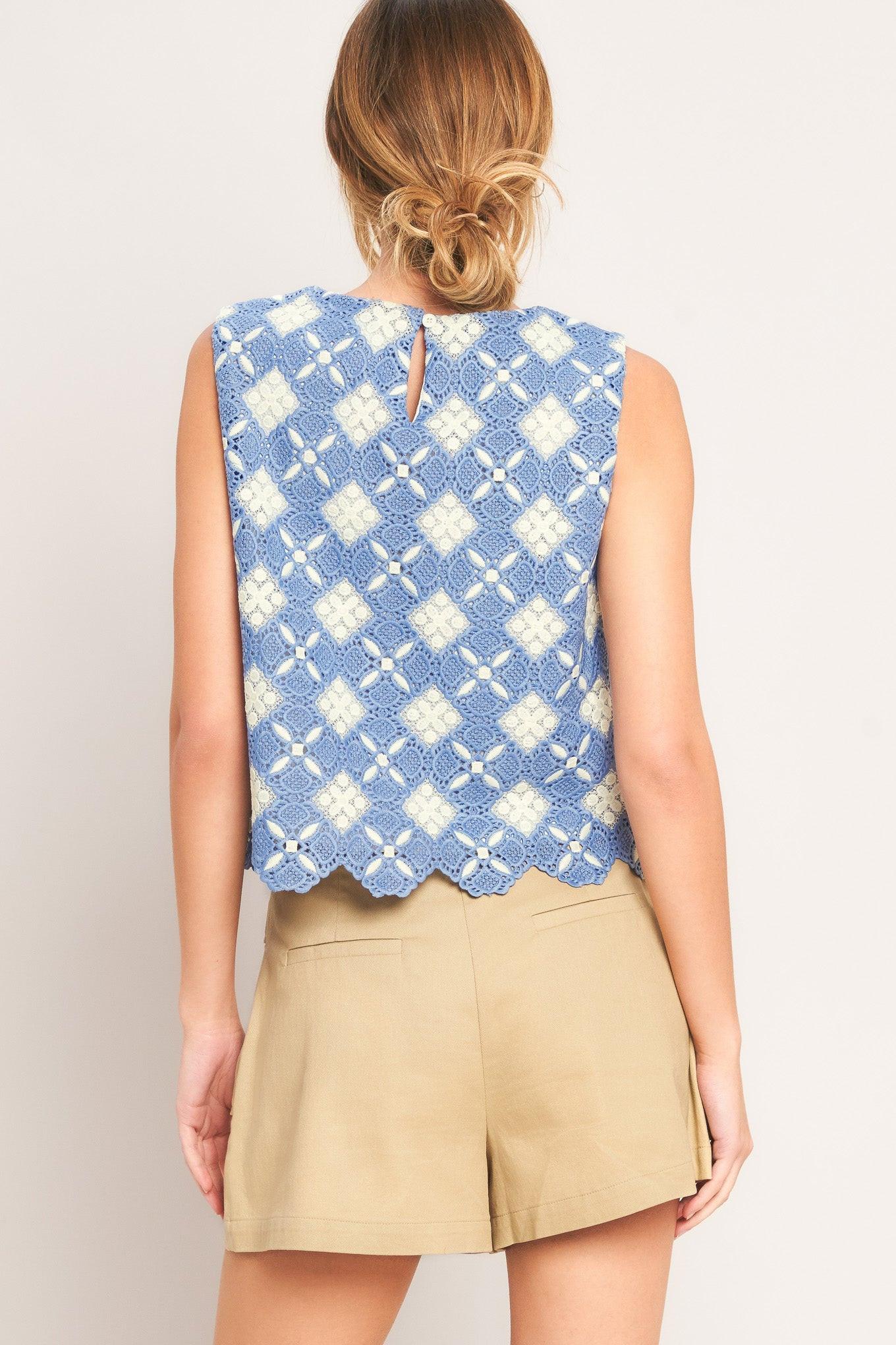 Woman wearing a sleeveless blue and white patterned top with beige shorts on a plain background