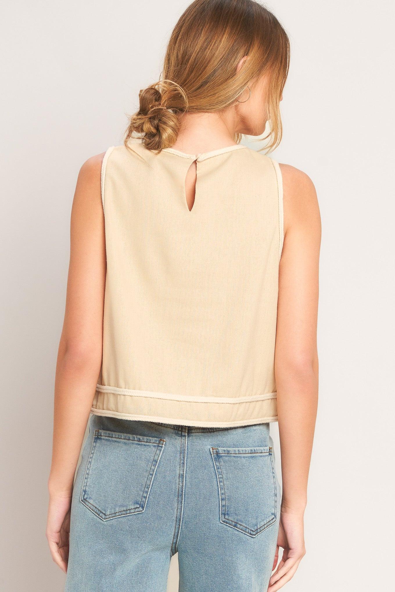 Woman wearing a beige sleeveless top and blue jeans against a plain background