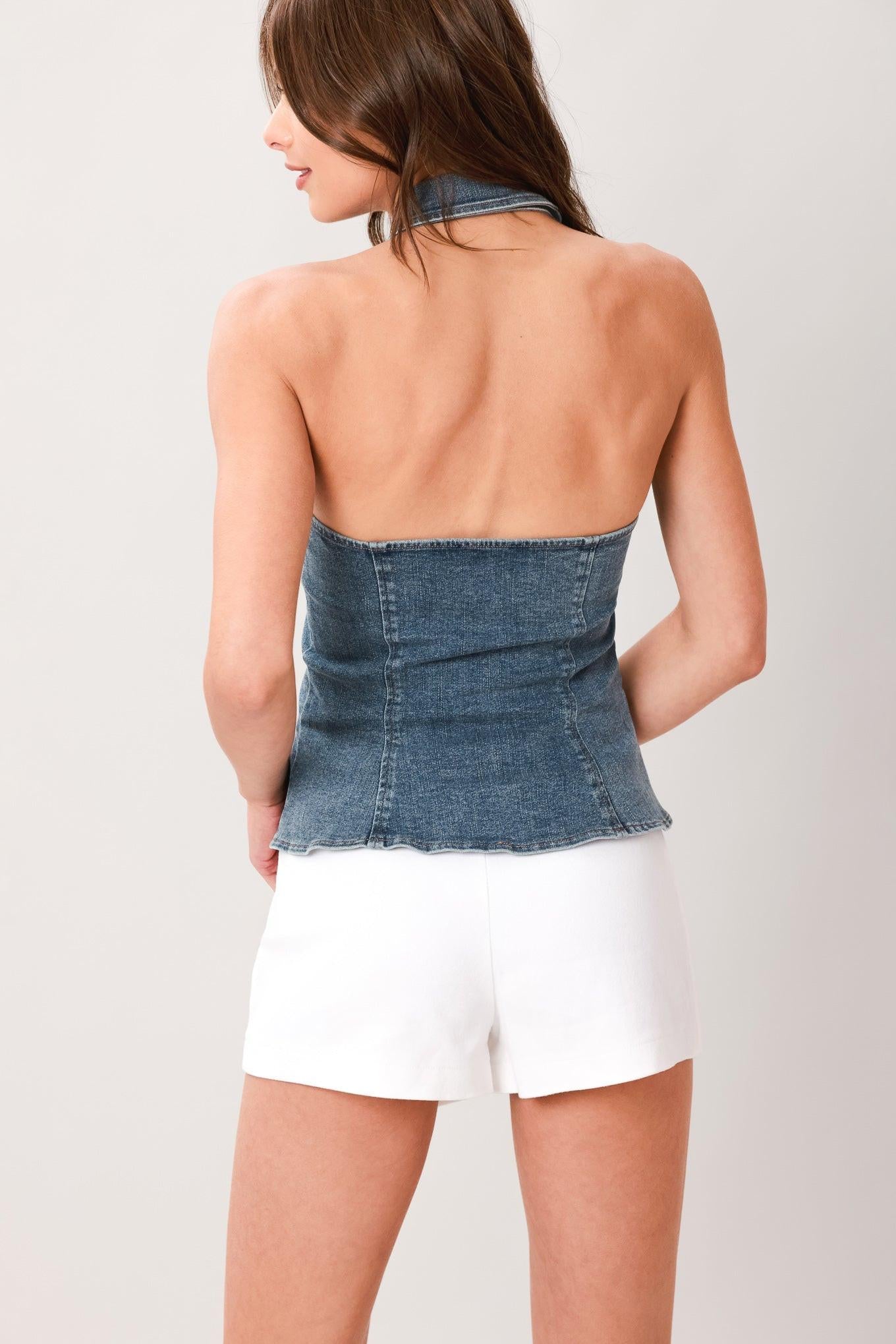 Woman wearing a washed denim top featuring halter neckline with collar, ruffle placket, button down and bare back