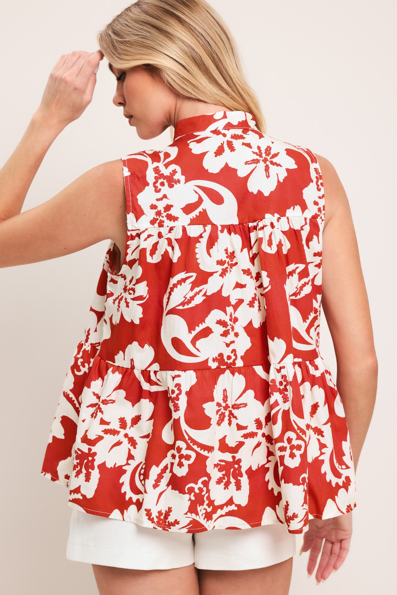 Woman wearing a red and white floral sleeveless top with tiers and front button closure | Flying Tomato