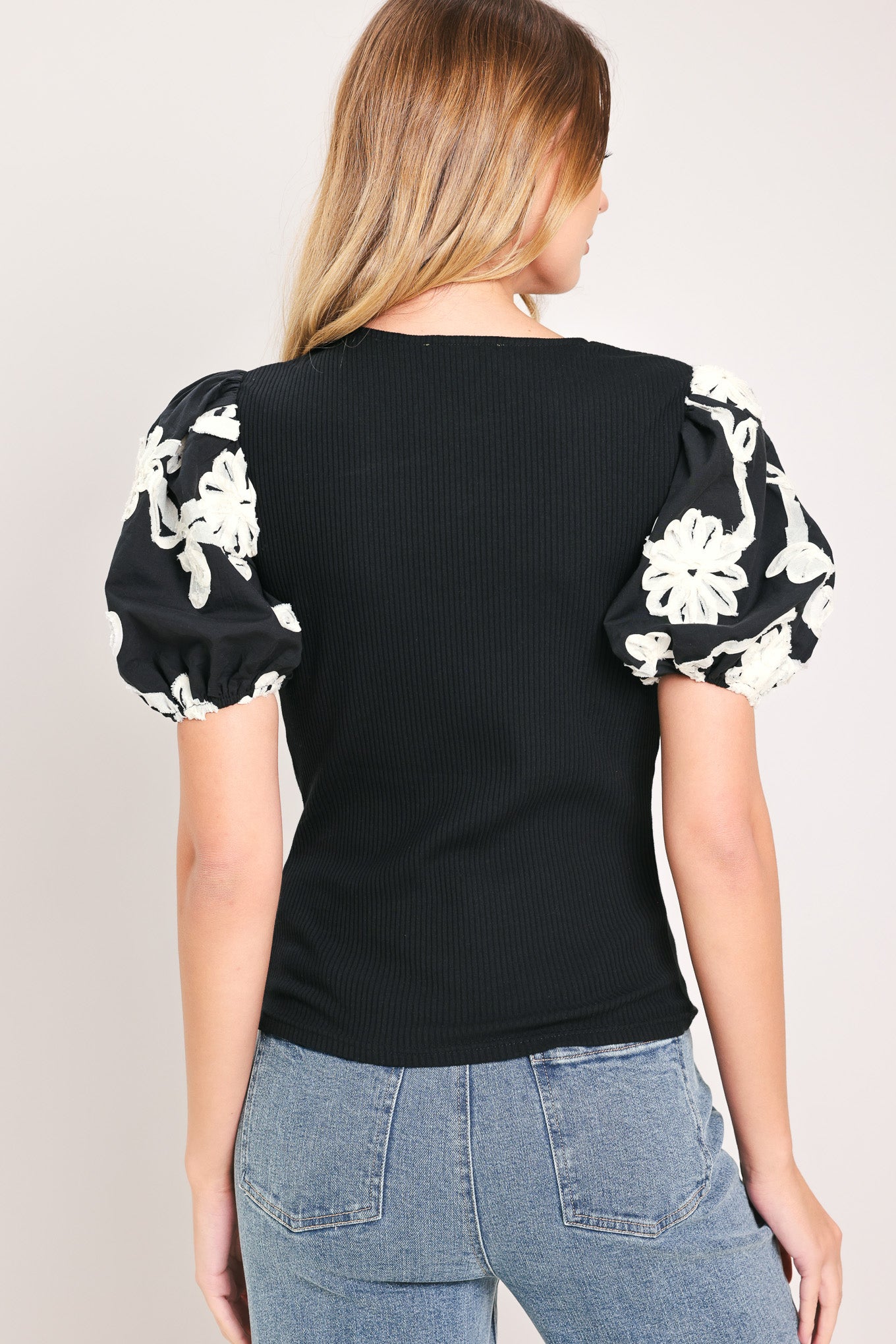 Woman wearing a black ribbed knit top with V neckline and short puff embroidered white floral sleeves | Flying Tomato