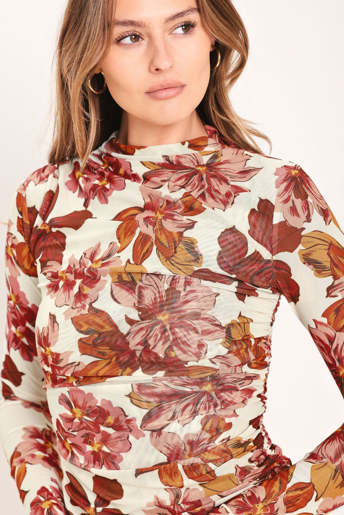 Woman wearing a long sleeve ivory and mauve floral printed woven mesh top with funnel neckline, side shirring | Flying Tomato