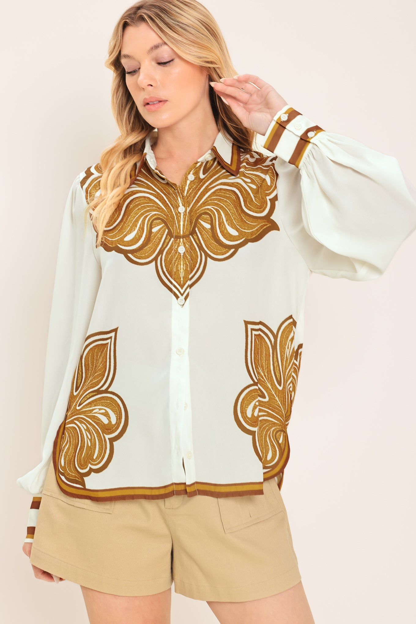 Woman wearing a white long sleeve button down blouse with brown leaf-like print | Flying Tomato