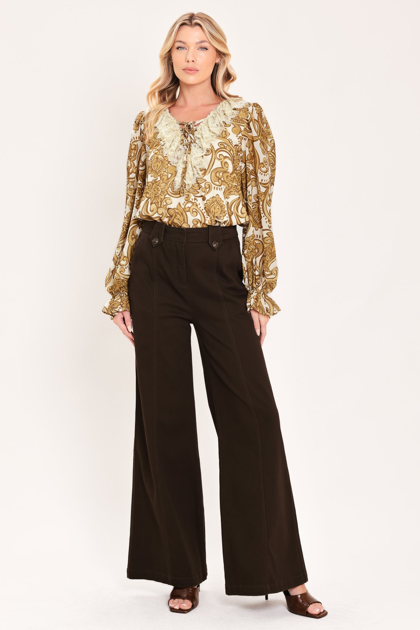 A woman wearing a long-sleeve blouse with a gold and beige baroque-style pattern, a ruffled lace-up neckline, and ruffled cuffs | Flying Tomato