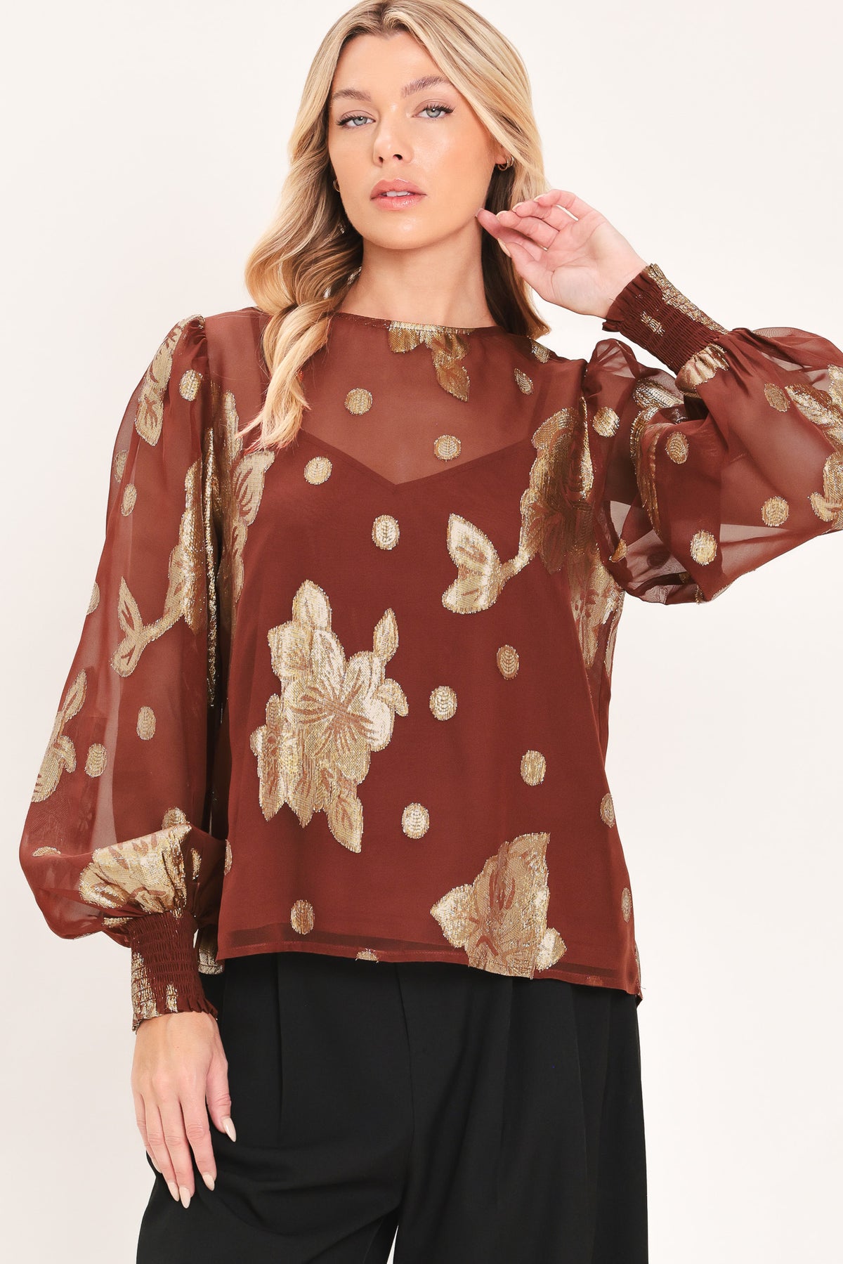 A woman wearing a sheer rust-brown/brick-colored blouse with metallic gold floral embroidery and puff sleeves | Flying Tomato
