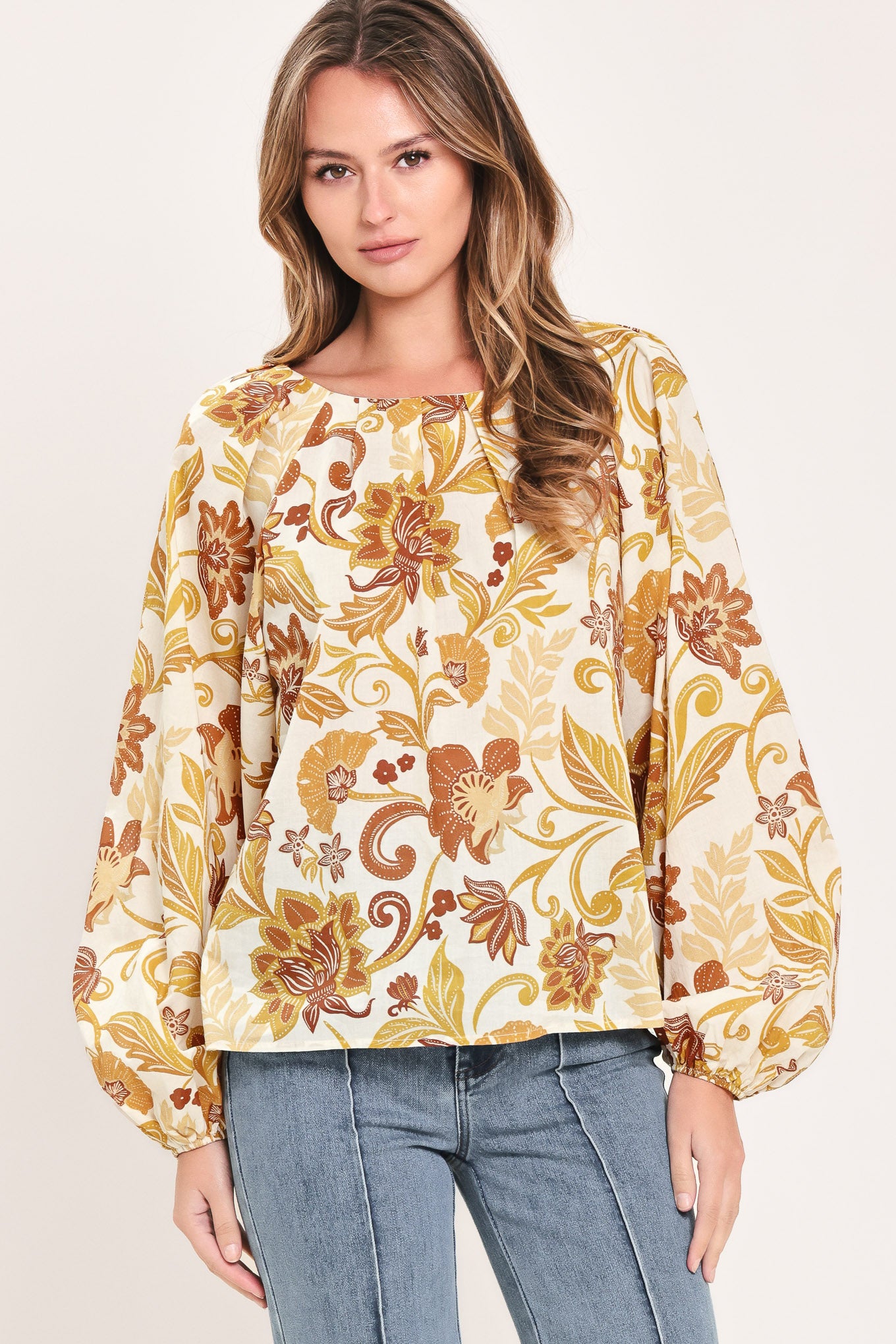 A woman wearing a long-sleeve blouse with a cream base and a brown and gold floral pattern | Flying Tomato