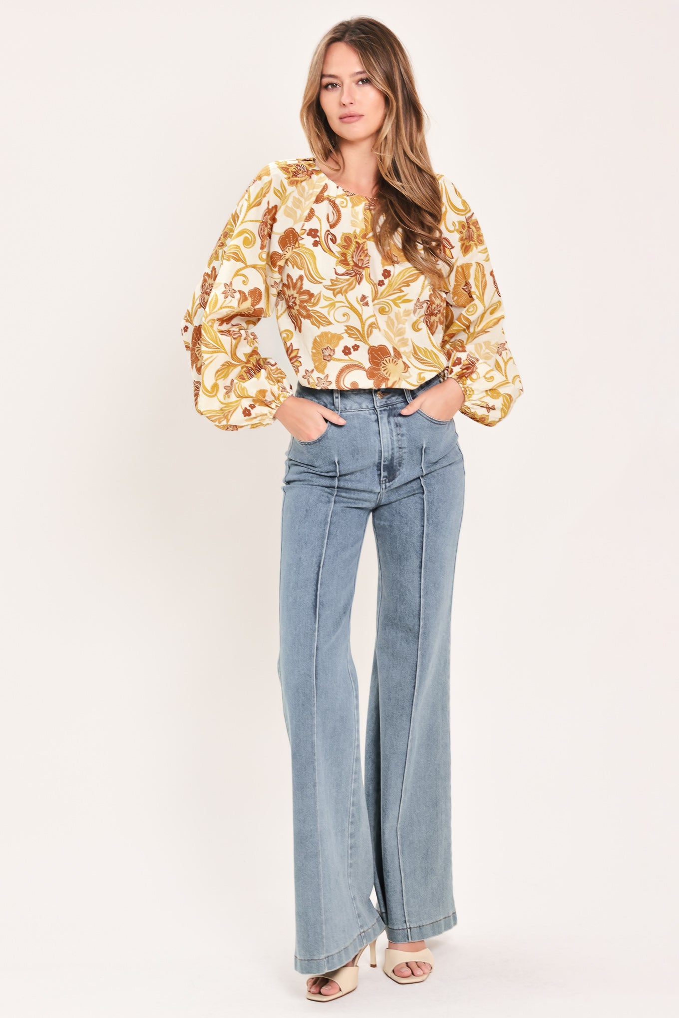 A woman wearing a long-sleeve blouse with a cream base and a brown and gold floral pattern | Flying Tomato