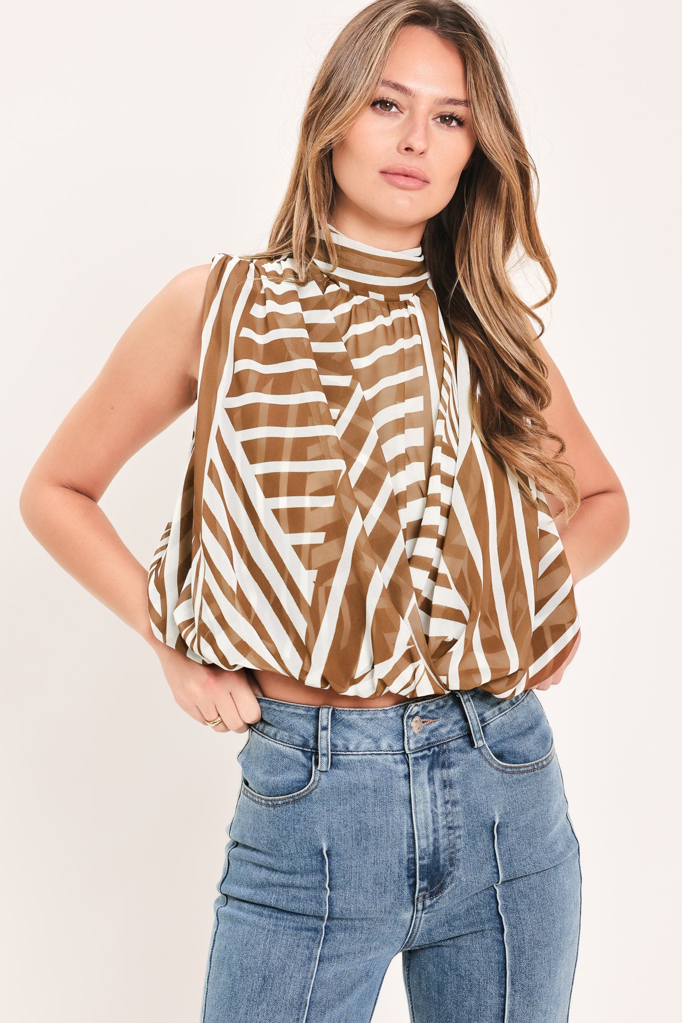 Woman wearing a sleeveless mocha and white geometric striped top with a high neck and flow silhouette | Flying Tomato